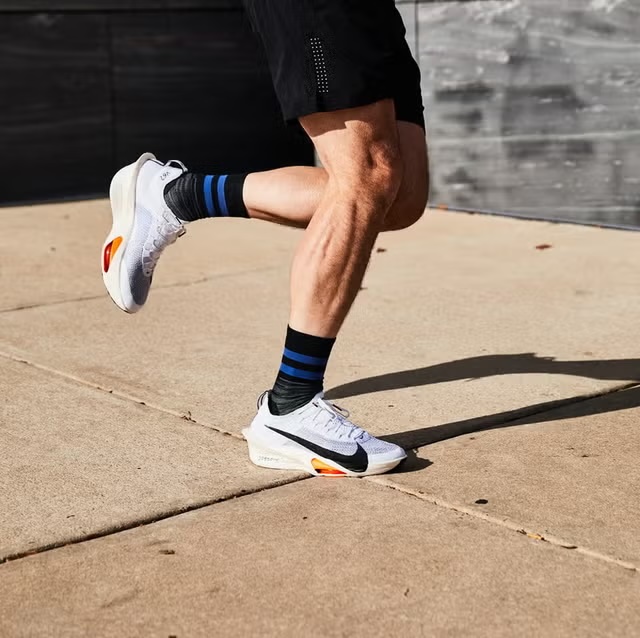 A runner mid-stride in white running shoes on a sunlit pavement