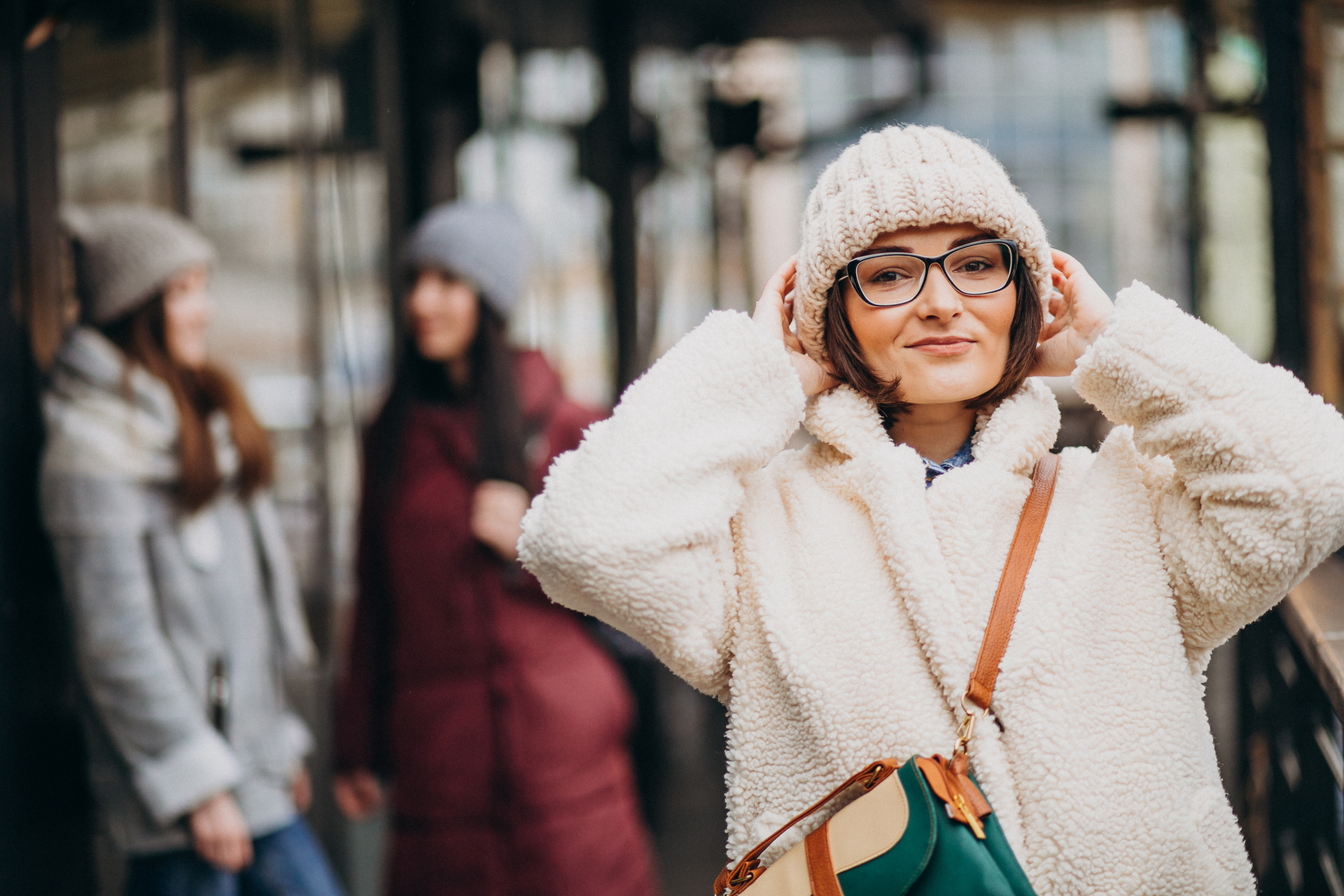 A shopper in a winter coat outside a row of storefronts, carrying a handbag